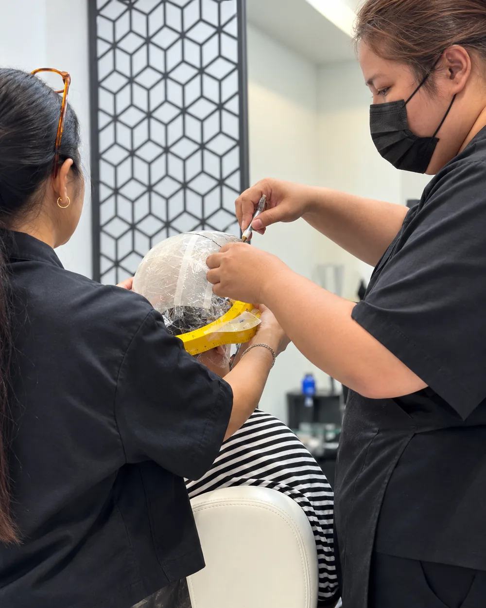 ช่างสองคนของร้านวิกผมผู้ชาย Wewigs Pro กำลังขึ้นโมศีรษะและใช้สายวัดวัดรอบศีรษะลูกค้าชาย ที่หน้าร้านจรัญสนิทวงศ์ 77 บางพลัด
