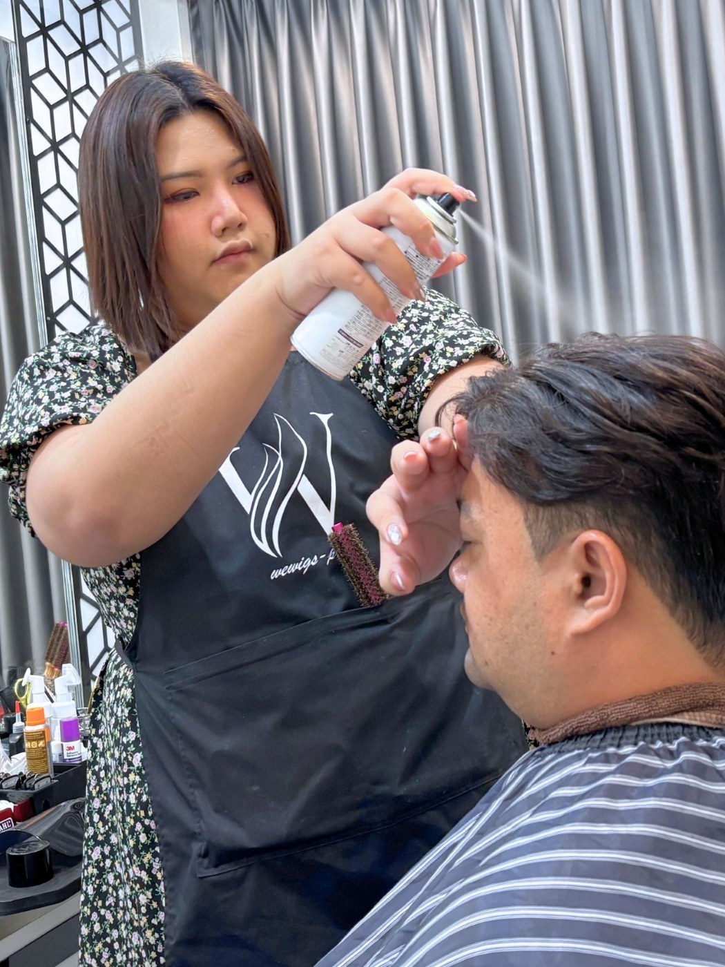 คุณอ้น ผู้เชี่ยวชาญด้านวิกผมของร้าน Wewigs Pro กำลังเซ็ตทรงและฉีดสเปรย์จัดแต่งแฮร์พีชผมแท้ให้ลูกค้าชายที่หน้าร้าน จรัญสนิทวงศ์ 77 บางพลัด