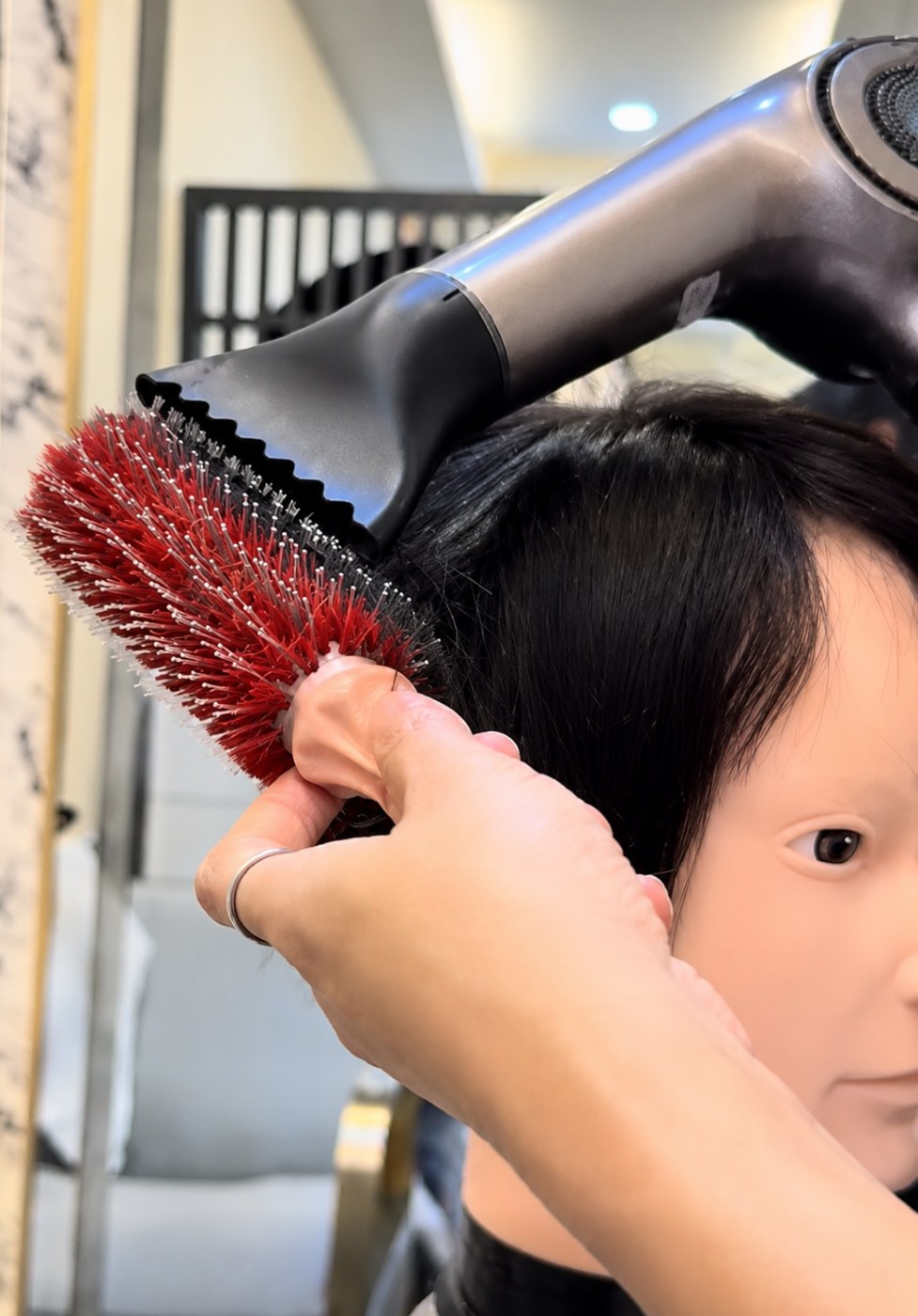 ช่างของร้านวิกผม Wewigs Pro กำลังเป่าแห้งและเซ็ตทรงวิกผมแท้บนหุ่นหัวด้วยแปรงกลม หลังเสร็จบริการซักและสปา