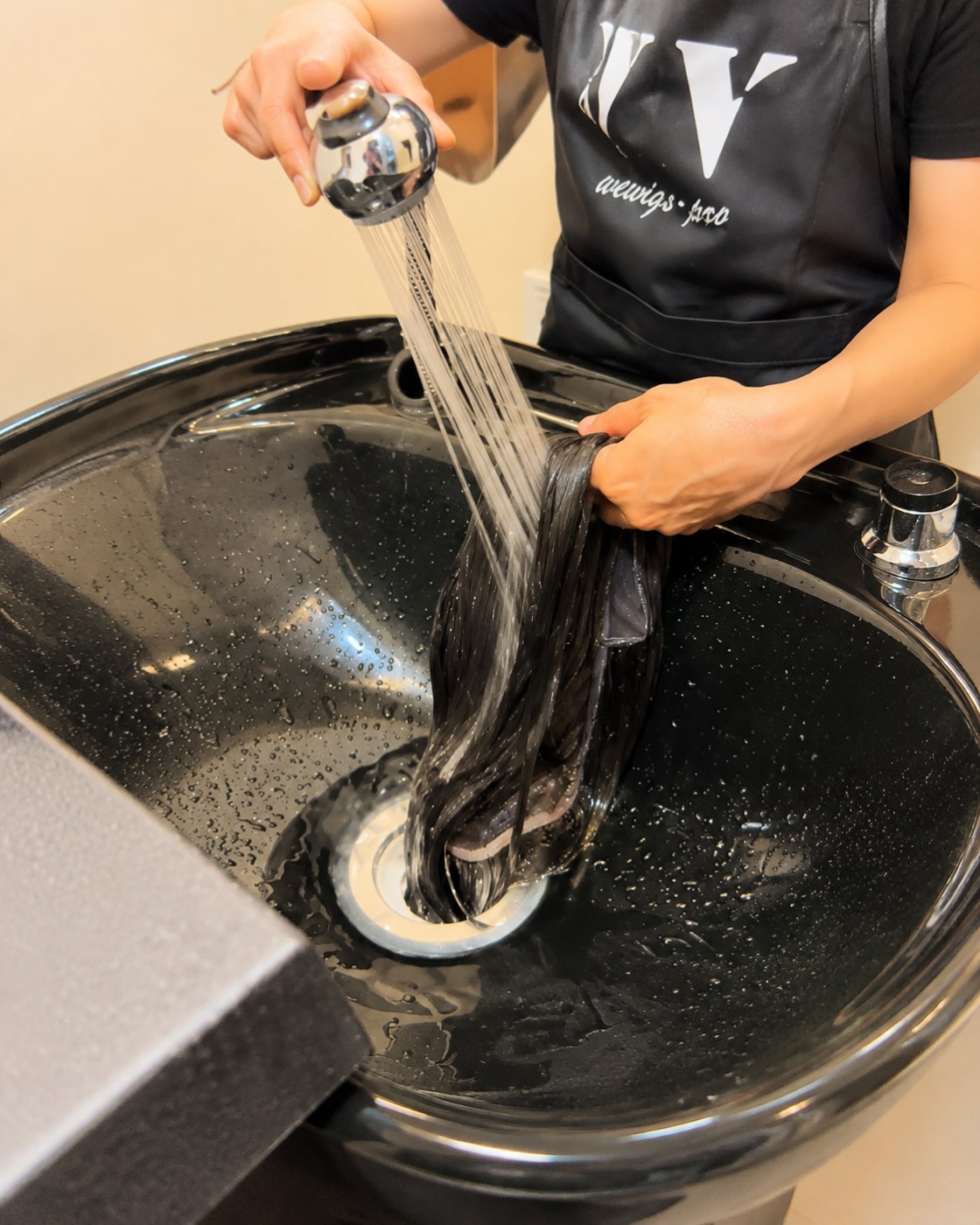 ช่างของร้านวิกผม Wewigs Pro กำลังสระวิกผมแท้ในอ่างสระของร้าน จับวิกให้เส้นผมไหลลงทางเดียวไม่ขยำ